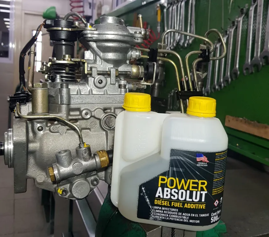 Bomba de inyección diésel en banco de taller junto a un envase de POWER ABSOLUT